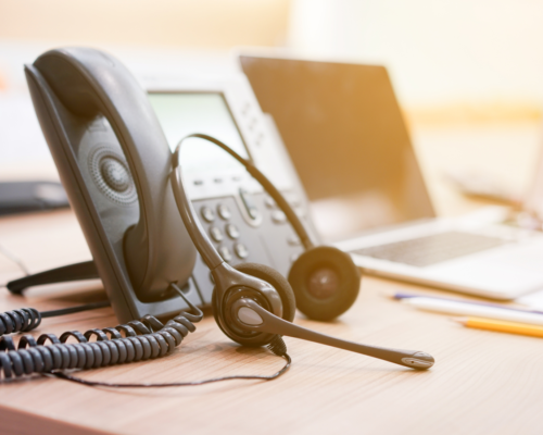 A work phone with a headset attached on a desk.