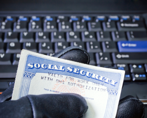 A gloved hand holding a social security card in front of a computer.