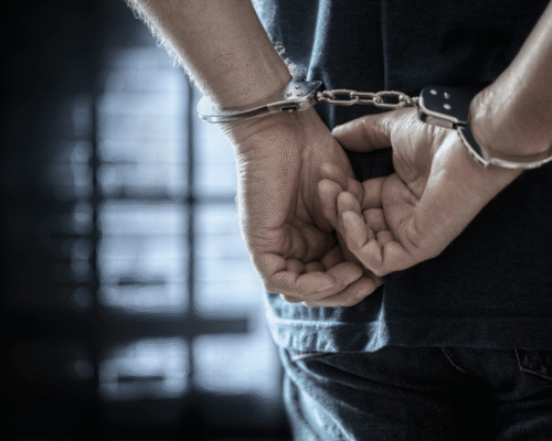 Arrested man in handcuffs with handcuffed hands behind back in prison