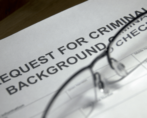 Close-up of a criminal background check request form with reading glasses resting on top, representing the impact of criminal records on employment opportunities and legal rights.
