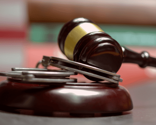 Judge’s gavel rests on a block beside metal handcuffs, symbolizing arrested vs indicted in criminal cases. The image reflects LA indictment process, arrest procedure California, grand jury indictment, criminal charges LA, preliminary hearing CA, and the criminal justice timeline.