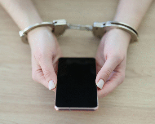 A person holding a smartphone while wearing handcuffs, illustrating how digital devices and communications can become central evidence in Los Angeles sex trafficking cases and criminal investigations.